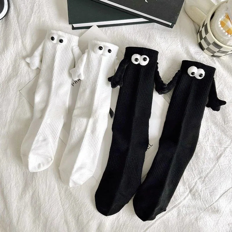 Cute ghost-themed socks with 3D googly eyes and flappy arms in black and white colors, placed on a cozy bed setting.